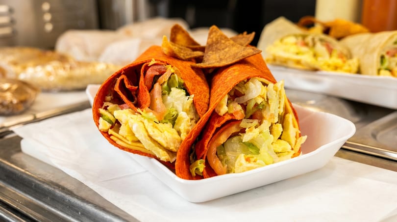 Two red wraps with egg, lettuce, and tomato, served with tortilla chips in a white takeout box.