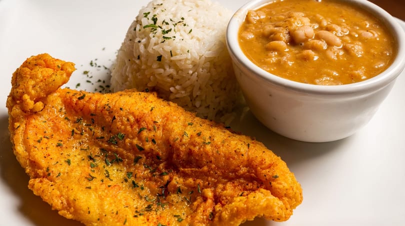 Crispy fried fish, fluffy white rice, and a bowl of creamy beans on a white plate.