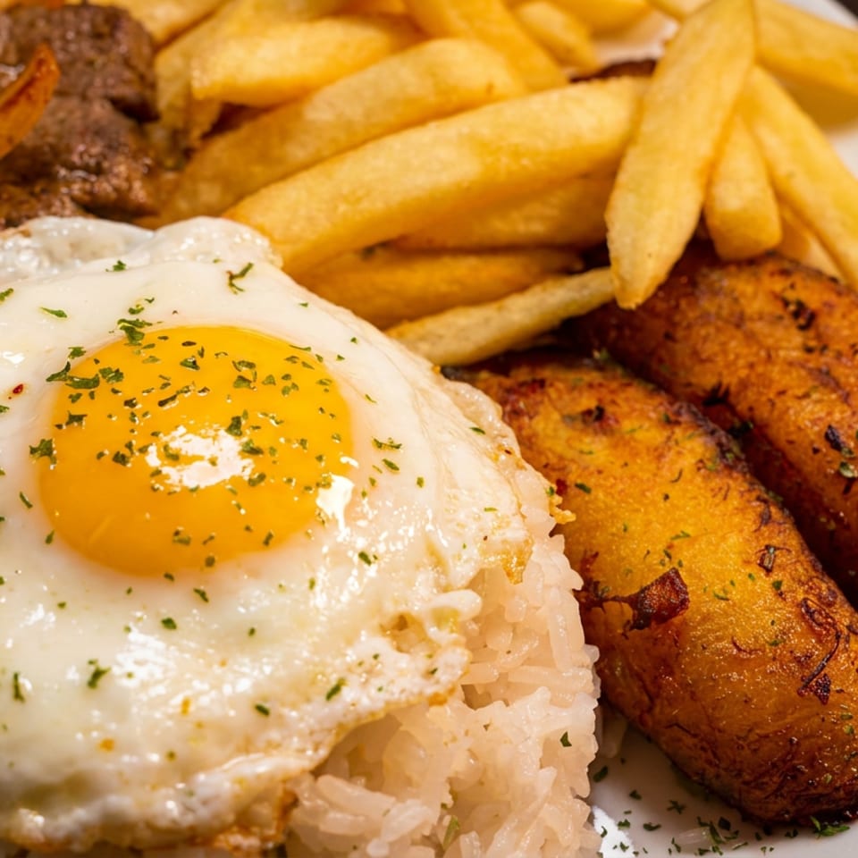 Hearty meal with fried egg, rice, steak, onions, french fries, and fried plantains.